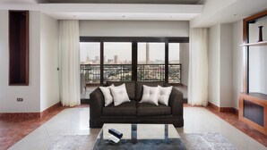 A modern living room with a dark sofa, a glass coffee table, and a city view through large windows. - VESTA  - Luxury APT - 4BR - Agouza (I) (Giza)