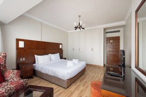 Ein Hotelzimmer mit einem Bett mit Holz-Kopfteil, weißen Laken, einem roten Ohrensessel, einem kleinen Tisch, einem Fernseher und einem Kleiderschrank.