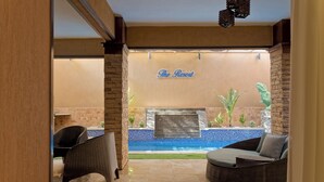 Lomakeskuksen sisätilat, joissa on rottinkihuonekaluja, uima-allasalue ja kyltti, jossa lukee: ”The Resort”.