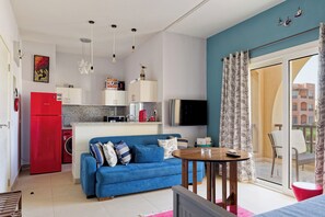 A compact living space with a kitchenette, a blue sofa, a dining table, and a balcony with a chair.