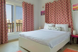A bedroom with a bed, curtains, a window, and a painting on the wall. - VESTA - Luxury APT - 1BR - Water Side Condos (El Gouna)