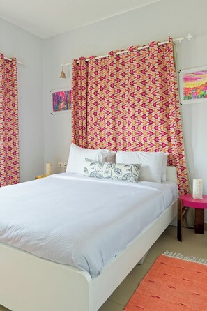 A bed with white bedding, a pink side table, and a colorful abstract painting on the wall.