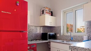Une cuisine compacte avec un réfrigérateur rouge, un four à micro-ondes, un lave-linge et une fenêtre donnant sur des immeubles.