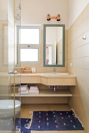 A bathroom with a glass shower enclosure, a sink with a mirror above it, and a window.