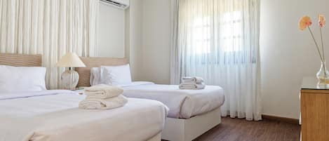 A hotel room with two beds, a bedside table with a lamp, a small vase with flowers, and a wooden nightstand.