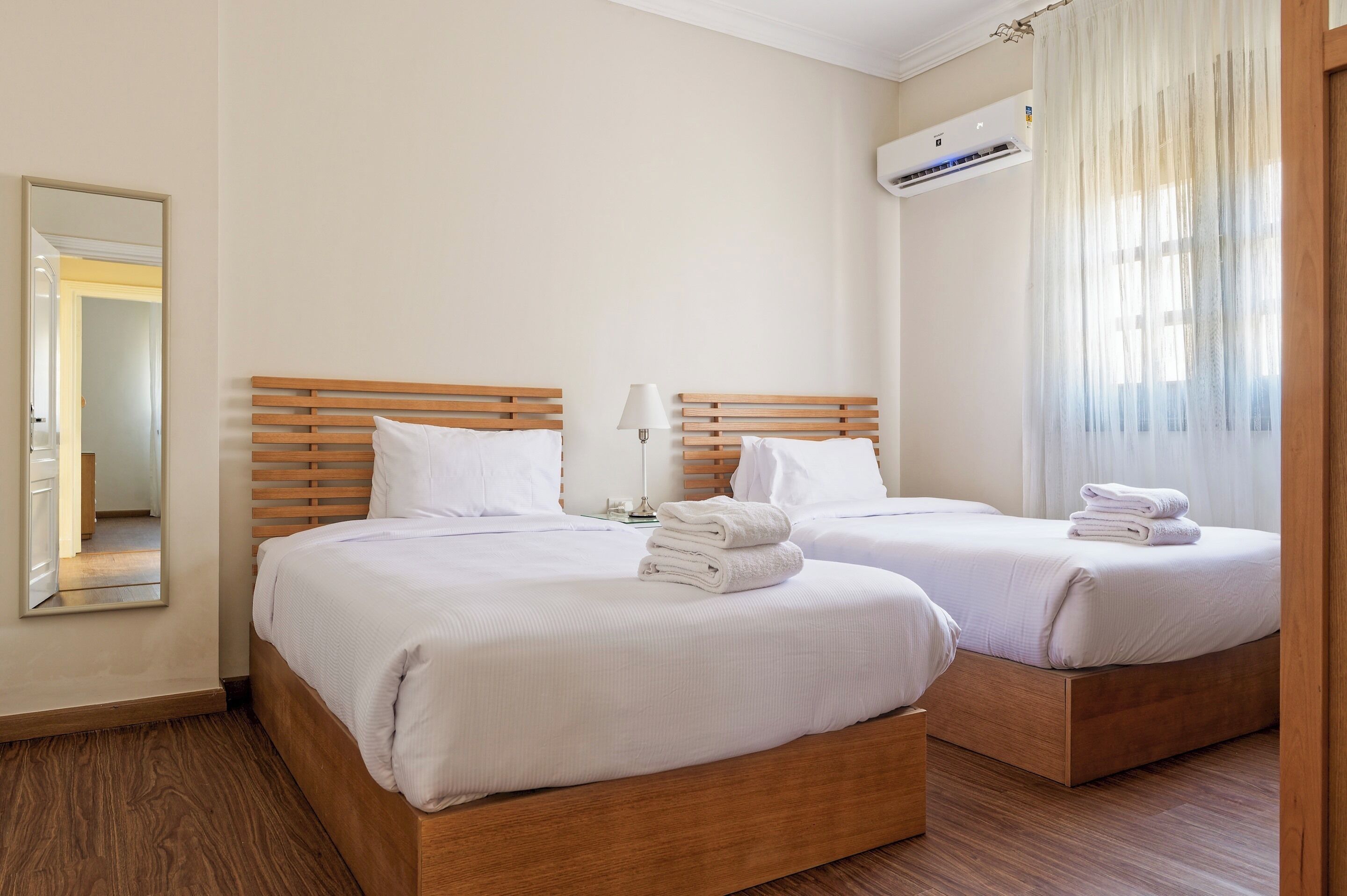 Une chambre d’hôtel avec deux lits, un miroir, un appareil de climatisation et une fenêtre avec des rideaux.