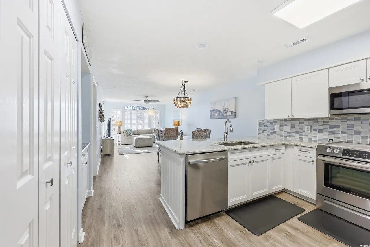 A modern kitchen with white cabinetry, a built-in dishwasher, a microwave, and a large island with a sink.