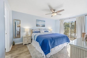 Una camera da letto con un letto, comodini, una ventola a soffitto, una finestra con tende e vista sull'esterno.