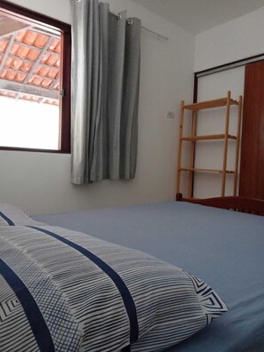 A bedroom with a bed, a window with curtains, and a wooden ladder against the wall.