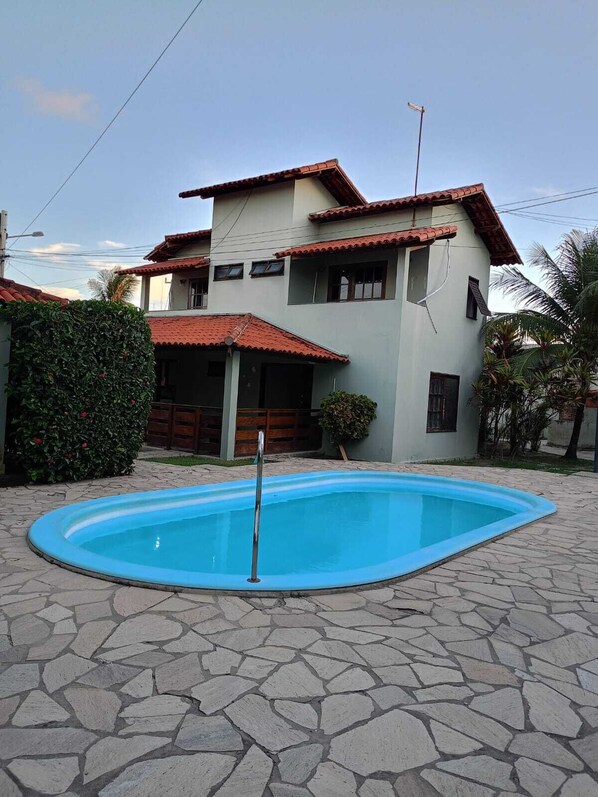 Ein zweistöckiges Haus mit Swimmingpool, Steinterrasse und einem roten Ziegeldach.