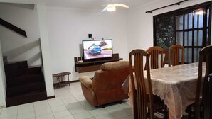 Un área de comedor con televisor, un sofá y una mesa con sillas.