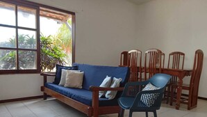 Una habitación con un sofá azul, sillas de madera, una mesa de comedor y una ventana con plantas afuera.
