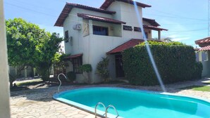 Una casa de dos pisos con piscina, patio de piedra y techo de tejas rojas.