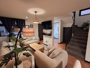 A modern living room with a sofa, coffee table, and hanging lamp. A staircase leads to an upper floor.