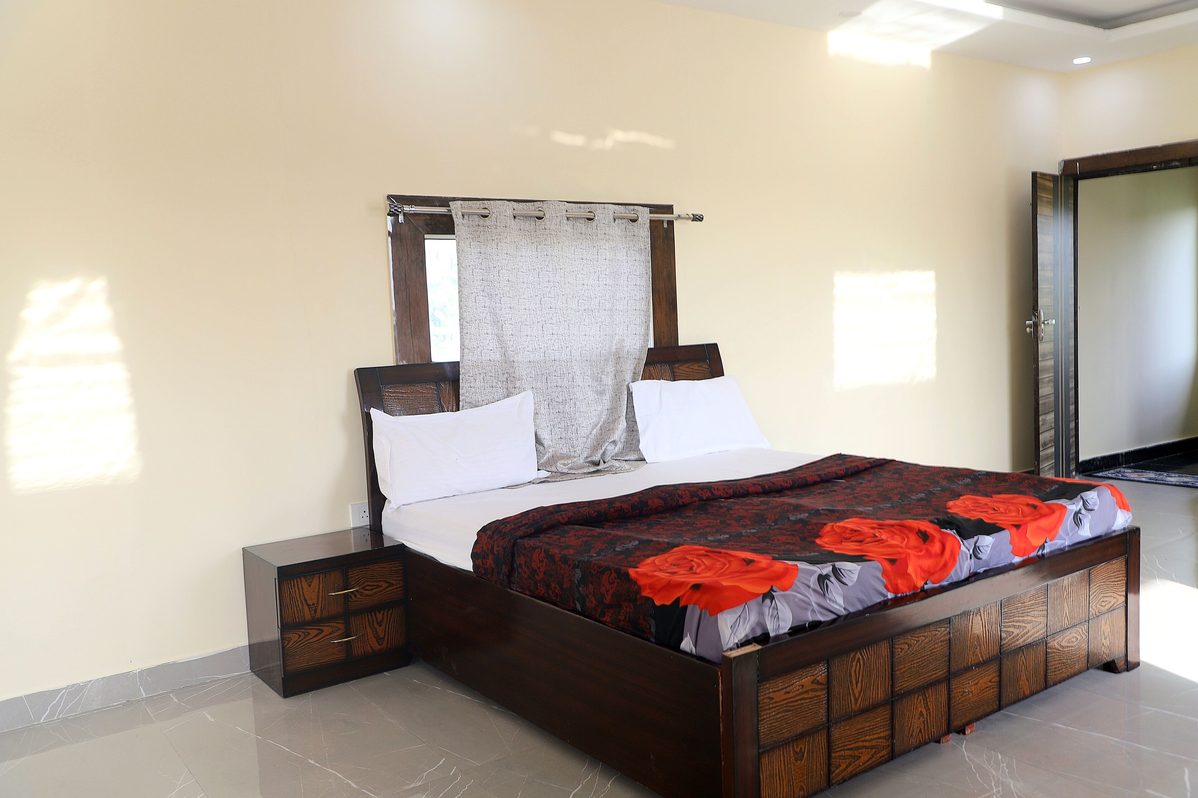 Una cama con estructura de madera, cabecera y colcha estampada con motivos florales.