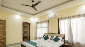 Une chambre à coucher avec un lit, un ventilateur de plafond, un appareil de climatisation, une porte en bois et des rideaux.