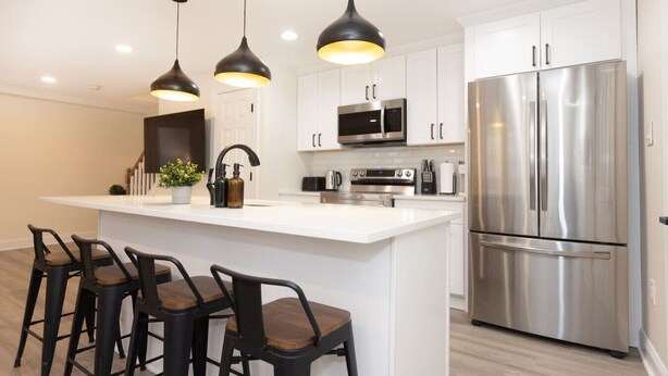 Una cocina moderna con una isla central, taburetes de bar, electrodomésticos de acero inoxidable e iluminación colgante.