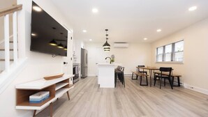 Una cocina moderna con horno integrado, una zona de comedor con mesa y sillas de madera, y un televisor montado en la pared.