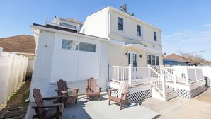 Una casa de dos pisos con fachada blanca, un porche con barandal blanco y tres sillas Adirondack.