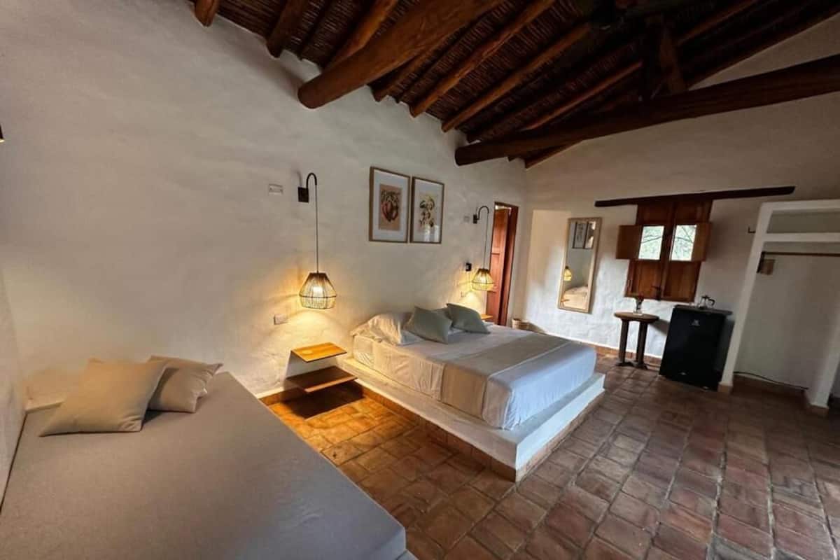 A bedroom with a bed, a sofa, a wooden ceiling, and a brick floor.