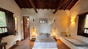 Una habitación con una cama, dos mesitas de noche, un banco e iluminación en la pared.