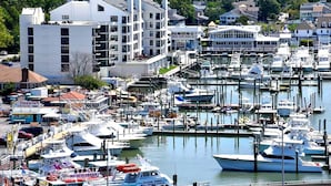 A marina with multiple boats docked, a white building with balconies, and a backdrop of residential houses. - Luxury Oceanfront 2BR 2BA Condo Private Balcony Beach Pool Full Kitchen Gym (Virginia Beach)