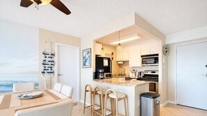 A modern kitchen with a central island, bar stools, and a view of the sea. - Luxury Oceanfront 2BR 2BA Condo Private Balcony Beach Pool Full Kitchen Gym (Virginia Beach)