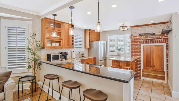 A kitchen with wooden cabinets, a central island with stools, a refrigerator, and a brick accent wall. - Annapolis Gem- Tranquil 4 BR Murray Hill Victorian (Annapolis)
