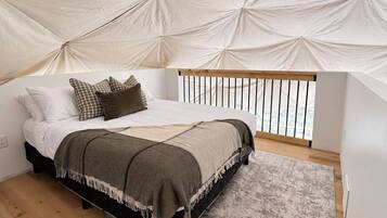 A bedroom with a bed, pillows, a blanket, a rug, and a tent-like structure above.