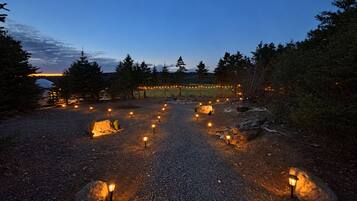 A gravel pathway with evenly spaced lanterns leading to a covered area with string lights.