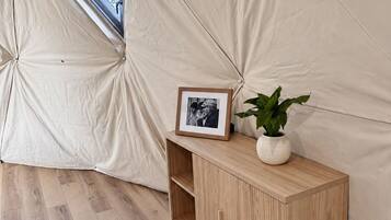 A tent interior with a wooden cabinet, a framed picture, and a potted plant.