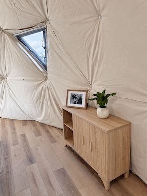 L'intérieur d'une tente avec un meuble en bois, un tableau encadré et une plante en pot.
