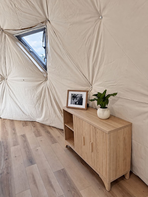 A tent interior with a wooden cabinet, a framed picture, and a potted plant.