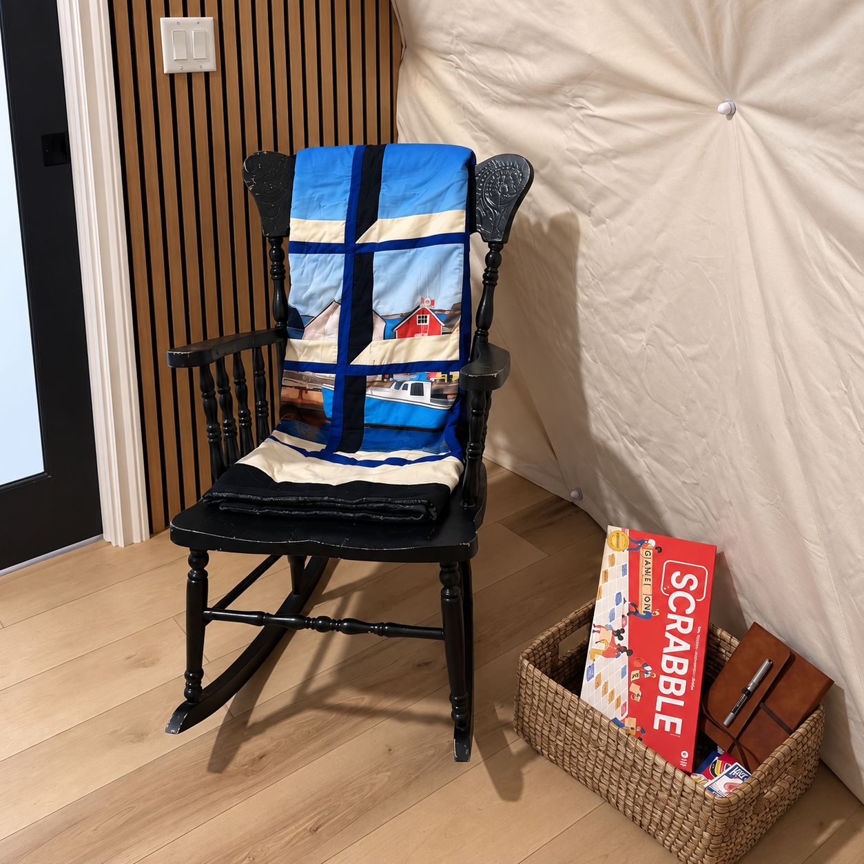 Una silla con un cojín estampado, una caja de juego de Scrabble y una libreta sobre una cesta tejida.