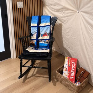 A chair with a patterned cushion, a Scrabble game box, and a notebook on a woven basket.