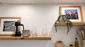 A kitchen with a coffee maker, glasses, a framed photo, a plant, and a bread loaf on a shelf.