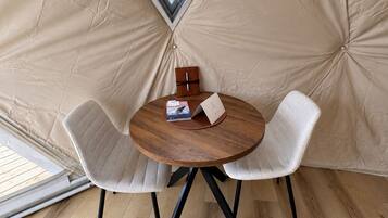 A tent with a round table and two chairs, a wooden box, and a booklet on the table.