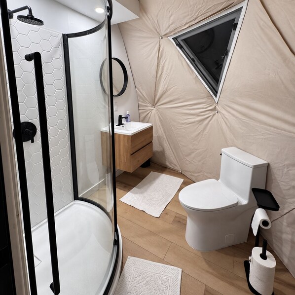 A compact bathroom with a shower, toilet, and sink, featuring a hexagonal tile pattern and a small window.