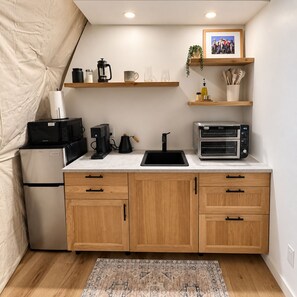 Eine kompakte Küchenzeile mit Kühlschrank, Mikrowelle, Kaffeemaschine, Toaster und Holzschränken.