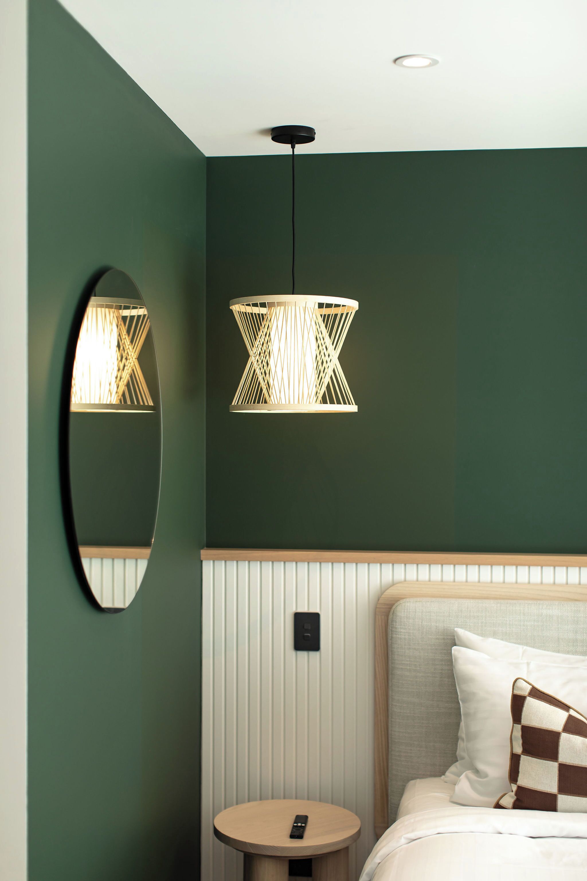 Une pièce comprenant un lit, une table ronde, un miroir et un luminaire suspendu.