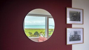 Un miroir rond reflétant un paysage de plage et d’océan, avec deux photographies encadrées accrochées au mur.
