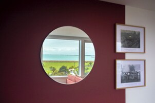 Un espejo redondo que refleja una vista de una playa y el océano, con dos fotografías enmarcadas en la pared.