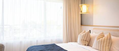 Habitación de hotel con cama, cortinas, lámpara colgante y vistas por la ventana.