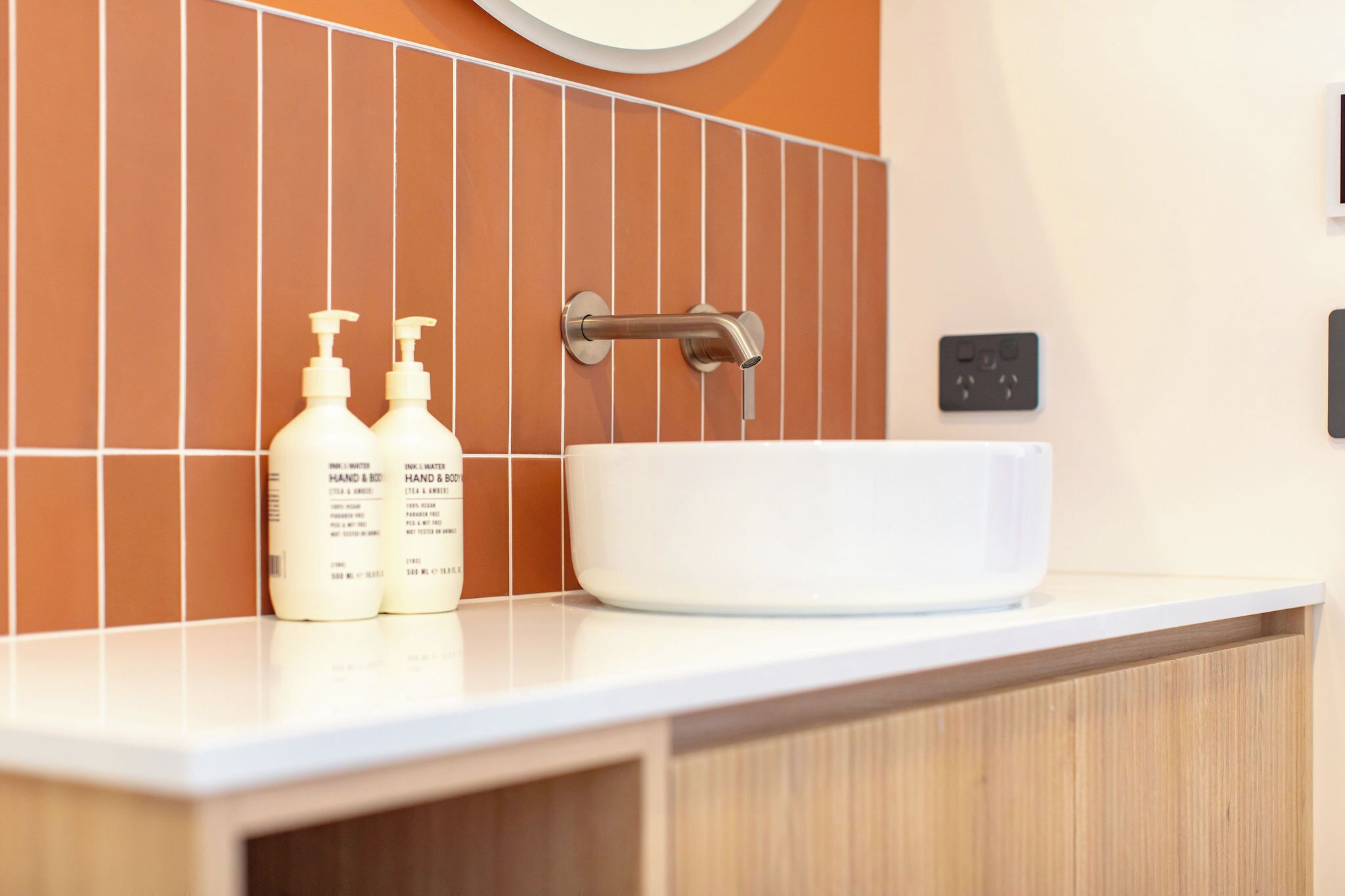 A bathroom with a white sink, two hand and body wash bottles, a towel rack, and a wall-mounted light switch.