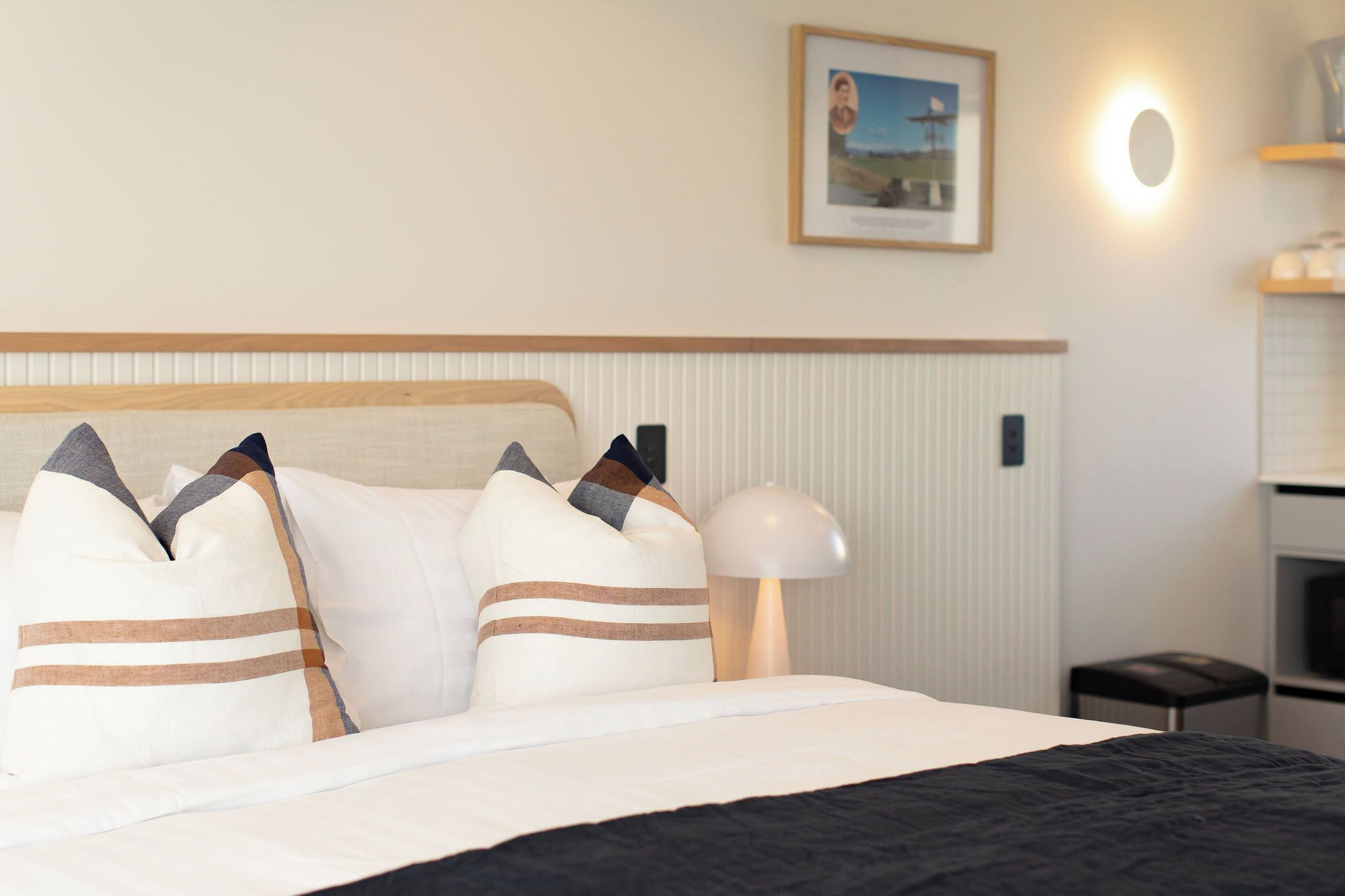A neatly made bed with striped pillows, a bedside lamp, and a framed picture on the wall.