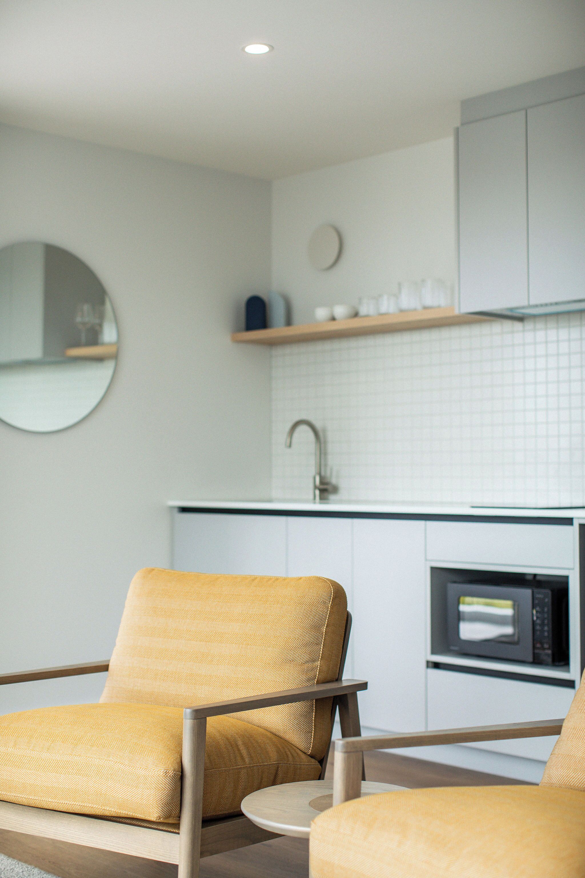 A modern kitchen with white cabinets, a microwave, and a round mirror on the wall.