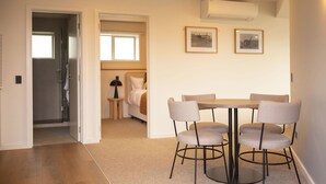 Une chambre moderne avec une table ronde et six chaises, un lit, une petite table de chevet et deux tableaux encadrés au mur.