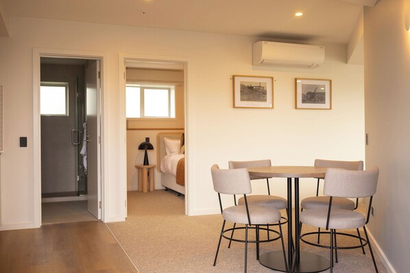 A modern room with a round table and six chairs, a bed, a small bedside table, and two framed pictures on the wall.