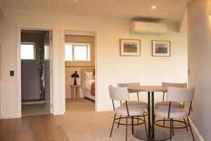 Una habitación moderna con una mesa redonda y seis sillas, una cama, una mesita de noche pequeña y dos cuadros enmarcados en la pared.