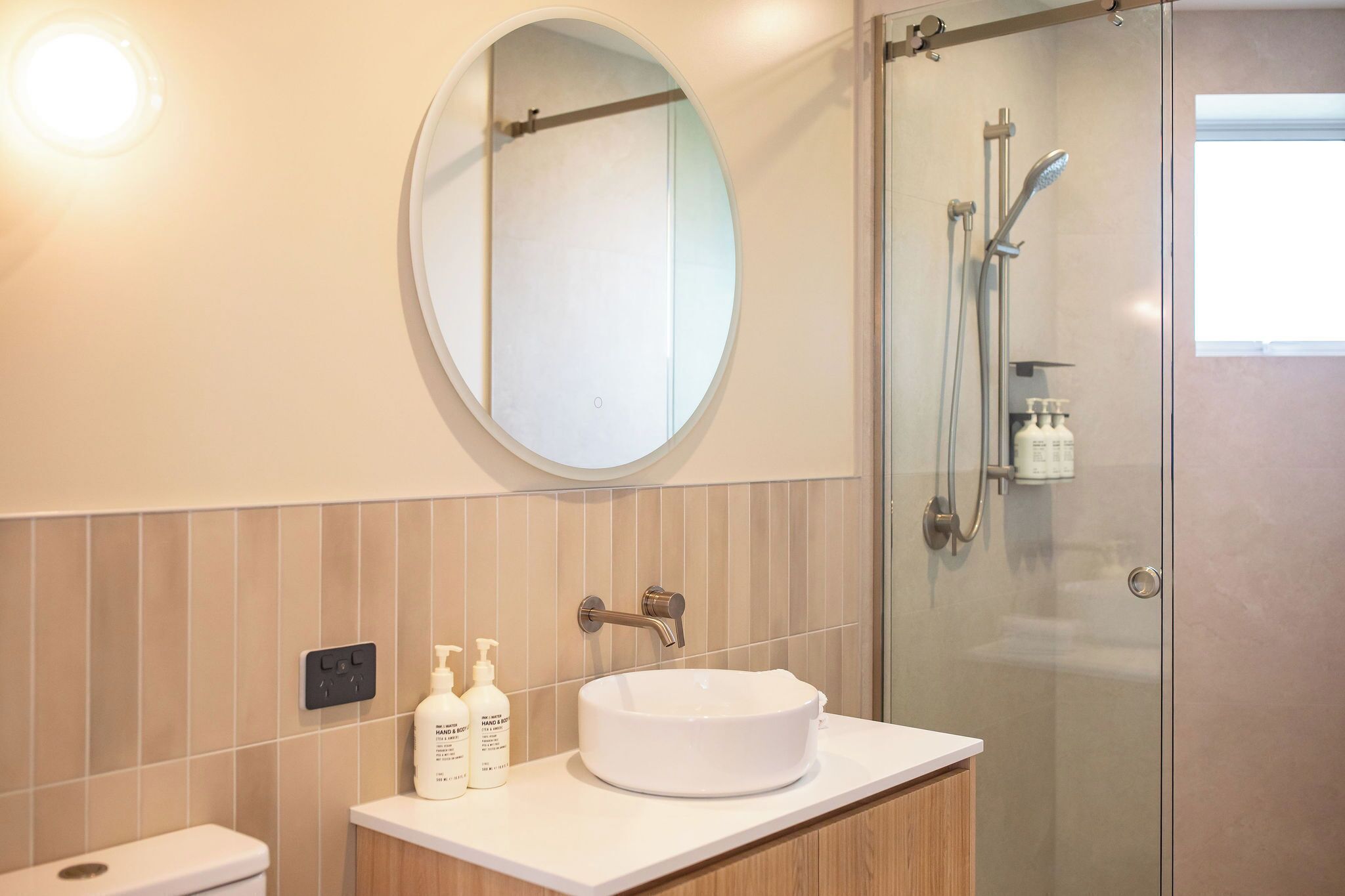 Un baño con un espejo redondo, un lavabo blanco, cabina de ducha de vidrio y un inodoro.